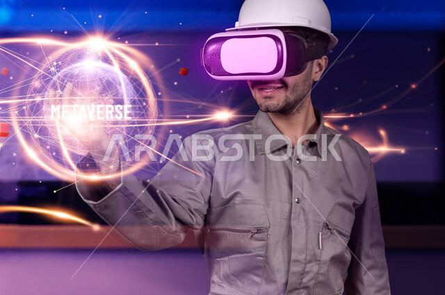 استخدام خاصية الهولوجرام ثلاثية الأبعاد، صورة مقربة لعامل صناعي عربي خليجي سعودي يرتدي الخوذة و زي العمل ونظارة الفي آر يتفاعل مع أيقونة الكرة الارضية الهولوجرامية في الواقع الافتراضي، تطور المجال العملي باستخدام التكنولوجيا والتقنيات الحديثة، خلفية ملونة