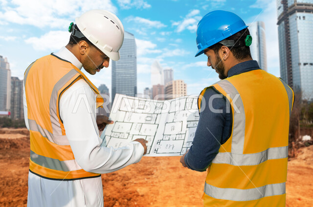Supervising and controlling engineering constructions, verifying the correct implementation of architectural projects, following up on the project and checking plans, a picture from the back of two Saudi Gulf Arab engineers wearing a helmet and work protective jacket discussing the construction plan, the background of the work site