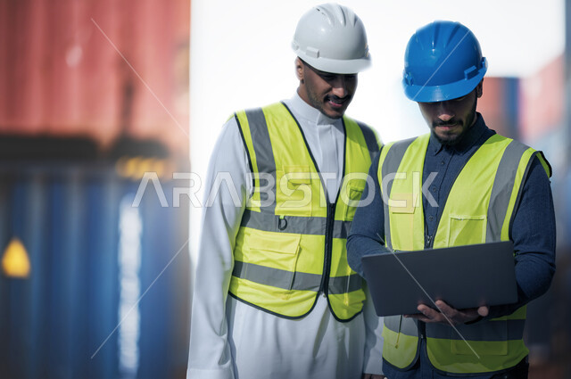 إعطاء تعليمات العمل من قبل المدير, مهندسان عربيان سعوديان خليجيان مبتسمان يقومان بالاشراف على توصيل ونقل الكونتينرات بإستخدام جهاز التابلت، استخدام الآلات المتطوره الحديثه في الإستيراد والتصدير, رؤية مستقبلية 2030، خلفية ميناء شحن البضائع و الحاويات التجاريه