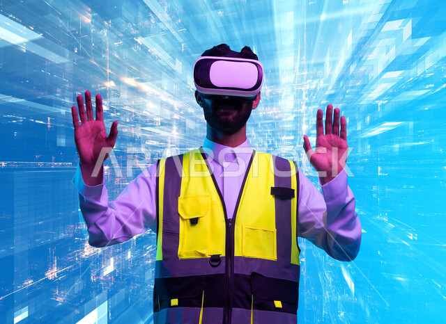The growth of the technological engineering field, interaction with virtual engineering, a close-up portrait of a Saudi Gulf Arab engineer wearing a work jacket and VR glasses interacting with holographic indicators and engineering graphic lines, working in the engineering sector via virtual reality technology, blue background