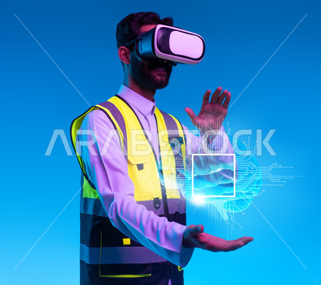 التفاعل مع الهندسة الافتراضية، بورتريه مقرب لمهندس عربي خليجي سعودي يرتدي سترة العمل ونظارة الفي آر يمسك بيده مجسمات ورسومات هولوجرامية، العمل بالقطاع الهندسي عبر تقنية الواقع الافتراضي،  نمو المجال الهندسي التكنولوجي، خلفية زرقاء