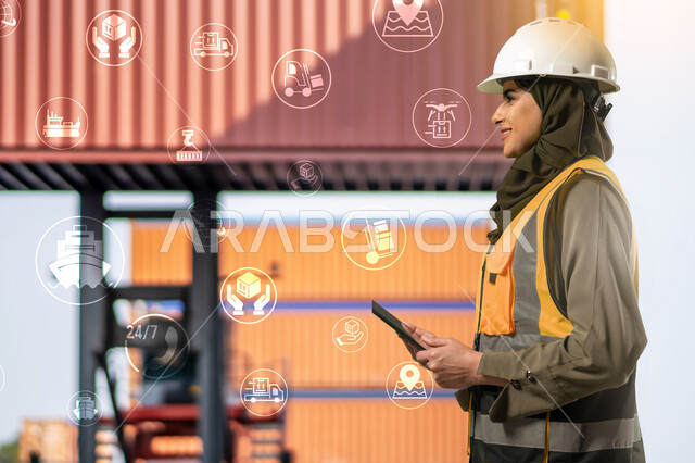 المتابعة  والإشراف على العمل عبر جهاز التابلت, صورة من الجانب لمهندسة صناعية عربية خليجية سعودية ترتدي الخوذة وسترة الحماية داخل المصنع، مشاركة النساء السعوديات في مجال الصناعة والهندسة، خلفية أيقونات بتقنية الهولوجرام