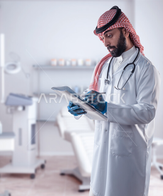 تشخيص الحالات المرضية, جراحة الفم ومفهوم طب الأسنان, طبيب عربي خليجي سعودي يرتدي المعطف الطبي الأبيض وسماعة الفحص يقوم بتسجيل المعلومات بملفات المرضى, تقديم الخدمات العلاجية, استخدام اجهزة تقنية طبية لفحص اسنان المريض, خلفية العيادة السنية