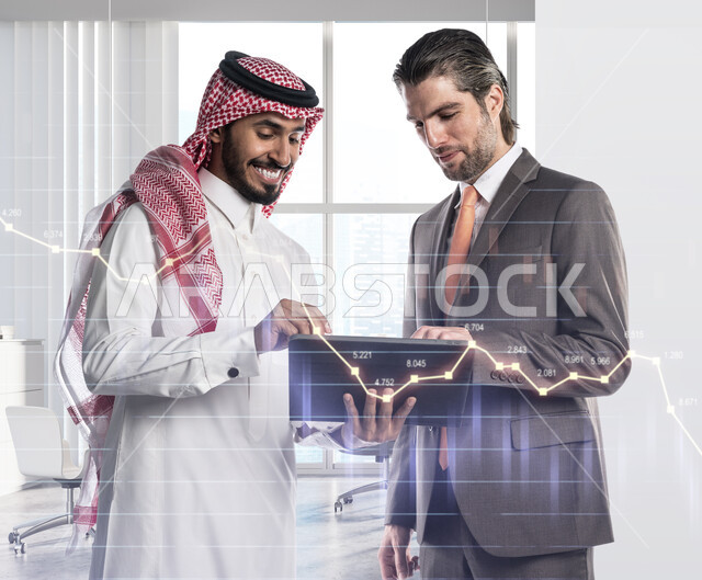 الوقوف بإيماءات السرور والحماس لزيادة تداول الأرباح المالية, مراقبة الاقتصاد عبر الرسم البياني للسوق السعودية, زملاء عمل عربييان خليجيان سعوديان يقومان بمراقبة صعود وهبوط أسهم البورصة عبر جهاز التابليت، تطوير استراتيجة العمل وتبادل الأفكار