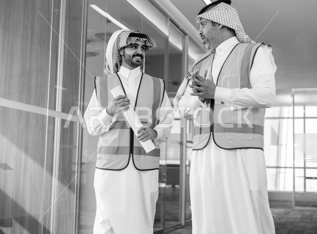 الاشراف على تطبيق المشاريع و الخطط الهندسيه, التشاور والحوار في إنجاز العمل واقتراح افكار جديده, صورة بالأبيض والأسود لمهندسين عربين خليجين سعوديين يرتديان سترة الحماية في مقر الشركة, العمل في القطاع الهندسي