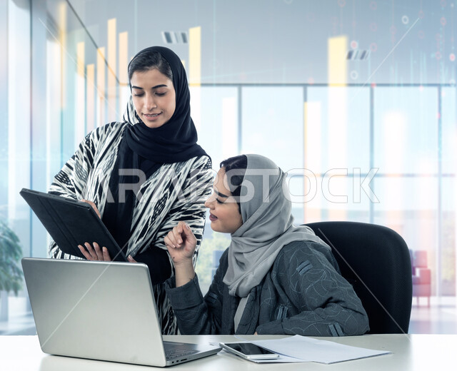 متابعة وإدارة الأعمال المكتبية, دمج العمل مع التقنية والتكنولوجيا, المناقشة والتشاور لتحقيق أهداف الشركة, امرأة عربية خليجية سعودية محجبة ترتدي العباءة تستخدم الأجهزة والتقنيات الحديثة برفقة زميلتها في المكتب, مهن ووظائف نسائية