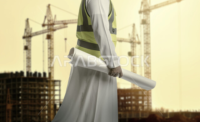 العمل في القطاع الهندسي، مفهوم الهندسة والانشاءات، الاشراف على تطبيق الخطط والمشاريع الهندسيه المعمارية، صورة مقربة بالأبيض والأسود ليد مهندس عربي خليجي سعودي يرتدي سترة الحماية يمسك مخطط البناء في مقر عمله، خلفية مبنى قيد الانشاء