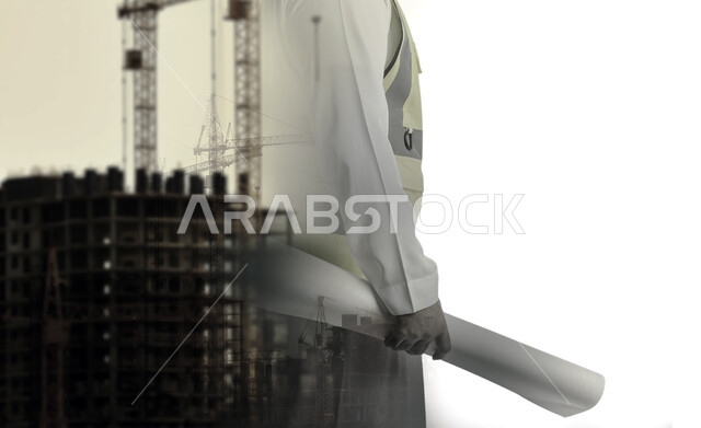 The concept of engineering and construction, working in the engineering sector, supervising the implementation of architectural plans and projects, a close-up black and white photo of the hand of a Saudi Arabian Gulf engineer wearing a protective vest holding a building plan at his workplace, background of a building under construction