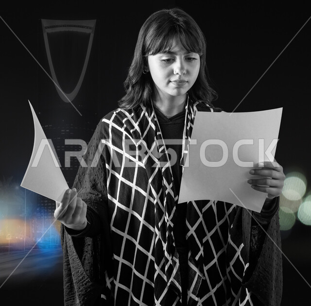 Using explanatory panels, an empty square white board, a black and white picture of a Saudi Gulf Arab young woman wearing a modern abaya, holding a white square mock-up in her hand, reading something with gestures of concentration and integration, against the background of the famous towers and skyscrapers in the Kingdom.
