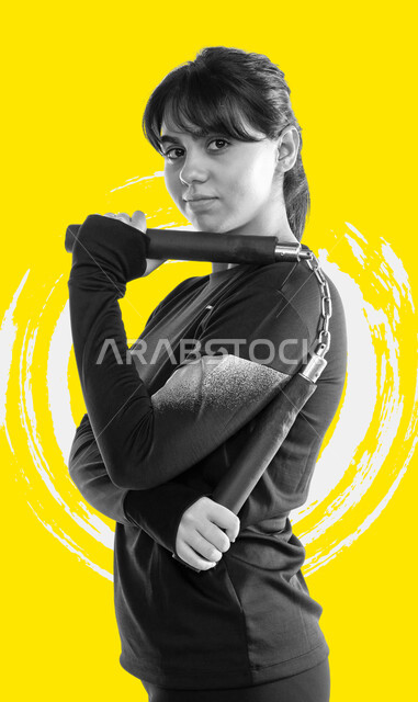 Learning the sport of self-defense, a side portrait of a Saudi Gulf Arab young woman holding a weapon and a nunchaku stick in her hand (Bruce Lee), training in combat movements, Japanese martial arts, looking at the camera with gestures of strength and confidence, the concept of Olympic Games sports, a healthy lifestyle, yellow background