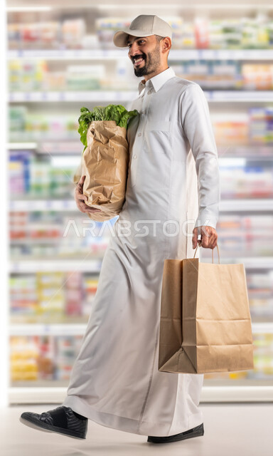 قضاء وقت ممتع في اختيار اللوازم المنزليه, امتلاك خيارات شراء واستهلاك مختلفة في السوبرماركت, السهولة والراحة في التسوق, رجل عربي سعودي خليجي يمشي في أحد أقسام الماركت ويحمل بيده الأكياس الورقية المليئة بالخضار