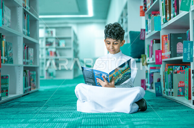 Reading entertaining pictorial stories, gestures of attention and concentration while reading, a Saudi Gulf Arab boy reading carefully in the library, spending his free time with learning and self-education, developing children’s reading skills, interest in browsing useful books