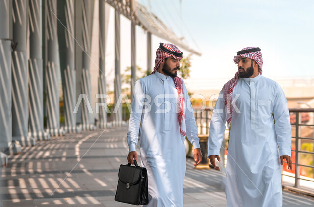 انتهاء الدوام و خروج الموظفين، رجلا أعمال عربيان سعوديان خليجيان يرتديان الشماغ والثوب التقليدي يتناقشان بإيماءات السرور، أصدقاء وزملاء عمل، مهن ووظائف سعودية، نقاشات وحوارات خارج مقر الشركة، شراكات عمل ناجحة