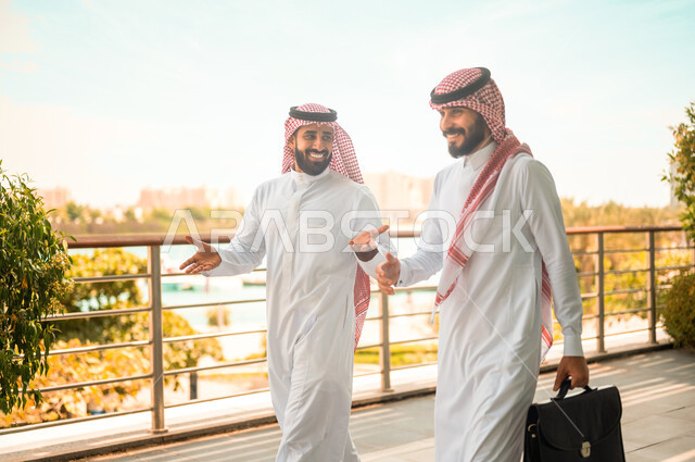 إنتهاء الدوام و خروج الموظفين، رجلا أعمال عربيان سعوديان خليجيان يرتديان الشماغ والثوب التقليدي يتناقشان بإيماءات السرور، أصدقاء وزملاء عمل، مهن ووظائف سعودية، نقاشات وحوارات خارج مقر الشركة، شراكات عمل ناجحة
