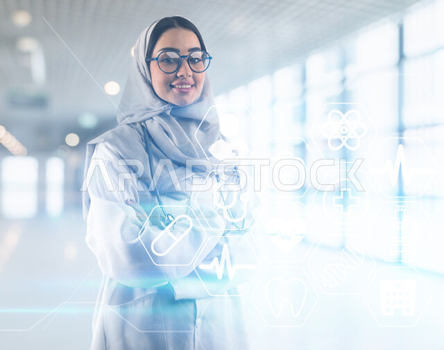 أيقونات طبية علمية بتقنية الهولوجرام, الاستعداد لتقديم الخدمات الصحية، العمل في القطاع الطبي, صورة مقربة لطبيبة عربية سعودية خليجية محجبة ترتدي المعطف الابيض ونظارات طبية تقف بأيدي متقاطعة, مفهوم الطب والرعاية الصحية، مهن ووظائف نسائية، خلفية ضبابية لمستشفى
