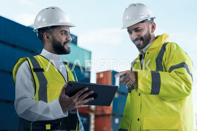 إعطاء تعليمات العمل من قبل المدير, ميناء شحن البضائع و الحاويات التجاريه، مهندسان عربيان سعوديان خليجيان مبتسمان يقومان بالاشراف على توصيل ونقل الكونتينرات بإستخدام جهاز التابلت، استخدام الآلات المتطوره الحديثه في الإستيراد والتصدير, رؤية مستقبلية 2030.