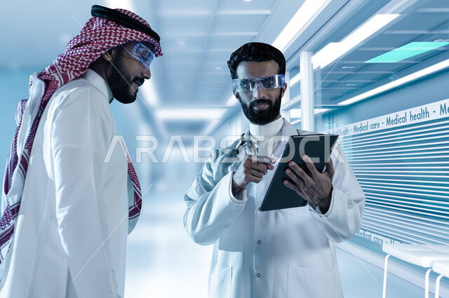 متابعة السجل الطبي الإلكتروني الخاص بالمريض من خلال جهاز التابلت, وصف الحالة المرضية وتقديم الاستشاره الطبية، طبيب عربي خليجي سعودي يرتدي المعطف الابيض والسماعة الطبية يتحدث مع المريض, مفهوم الطب وإعطاء العلاج المناسب للمرضى, خلفية المستشفى