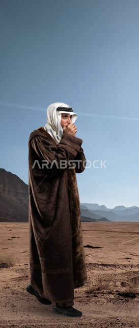 اسلوب الحياة في الصحراء، المشي و الحركة للحفاظ على دفئ الجسم في الاجواء الشتوية، رجل شايب عربي سعودي خليجي يرتدي الفروة الشتوية الدافئة ويضع العقال والغترة يقوم بالتنفس العميق في يديه لتدفئتها، إيماءات الشعور بالبرد الشديد.