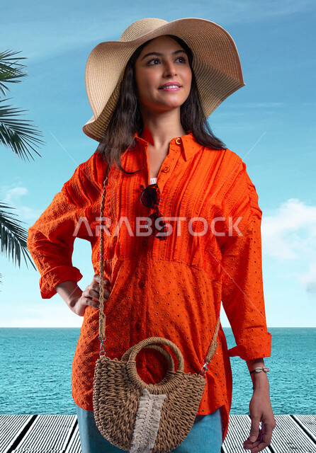 قضاء وقت ممتع على شاطئ البحر, مفهوم الأنوثة والأناقة، شابة عربية خليجية سعودية مبتسمة ترتدي القبعة والزي الكاجوال الخاص بالرحلات الصيفية تنظر إلى شيء ما، الوقوف بإيماءات الثقة والسعادة والسرور، جودة الحياة في الإجازة