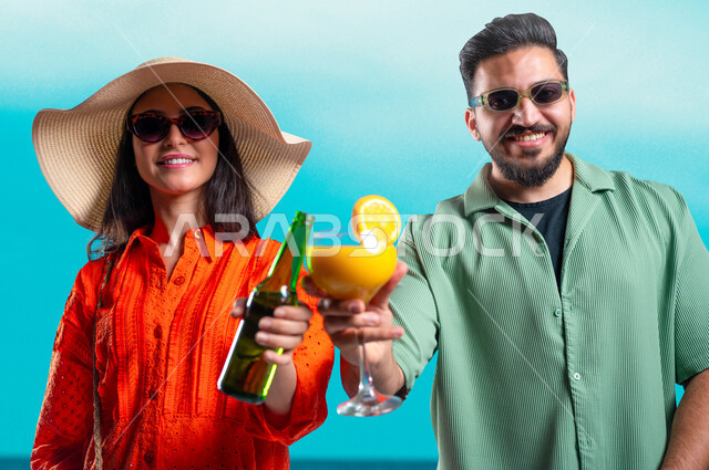 الاستمتاع بالمشروبات الباردة في الأجواء الحارة، النظر إلى الكاميرا بإيماءات السرور والسعادة، أجواء عائلية سعيدة, بورتريه مقرب لرجل وامرأة عربيين خليجين سعوديين مبتسمين يرتديان الزي الكاجوال والنظارات الشمسية يقومان بشرب العصائر المنعشة, خلفية زرقاء