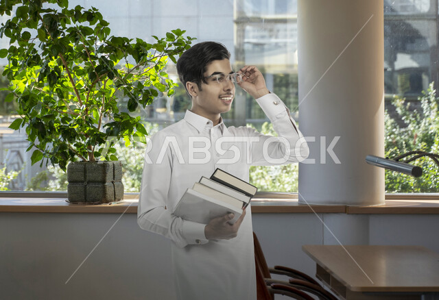 تطوير المناهج والمواد التعليمية في السعوديه، الاهتمام بجودة التعليم لتطوير المجتمع، طالب ثانوي عربي خليجي سعودي يرتدي الزي التقليدي يضع النظارة الطبية ويحمل بيده الكتب الدراسية، الالتزام بالدوام في المدرسة