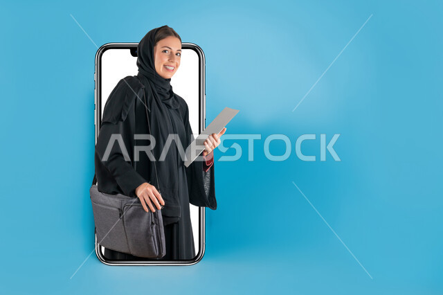التعليم في المدارس والجامعات السعودية، بورتريه لمجسم هاتف محمول بشاشة بيضاء كبيرة يخرج منه طالبة جامعية خليجية عربية سعودية مبتسمة ترتدي العباءة تحمل بيدها الكتب والحقيبة الدراسية، النظر إلى الكاميرا بإيماءات السرور، خلفية زرقاء