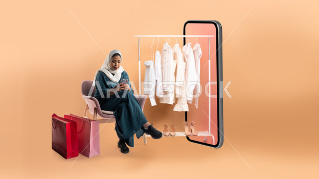 اقتناء المستلزمات والهدايا، بورتريه لإمرأة عربية خليجية سعودية ترتدي عباءة عصرية تجلس بجانب مجسم لهاتف محمول كبير بشاشة فارغة، علاقة ملابس تخرج من الهاتف، مفهوم الموضة والأناقة، التسوق والتبضع الالكتروني، خلفية بيج