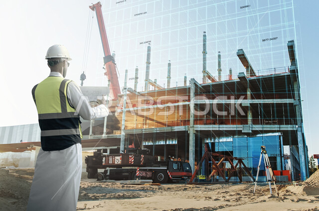 Working in the engineering sector, the concept of engineering and construction, supervising the implementation of architectural plans and projects in Saudi Arabia, a picture from the back of a Saudi Arabian Gulf engineer wearing a jacket and a protective helmet holding a building plan in his hand, comparison between plans and real work.