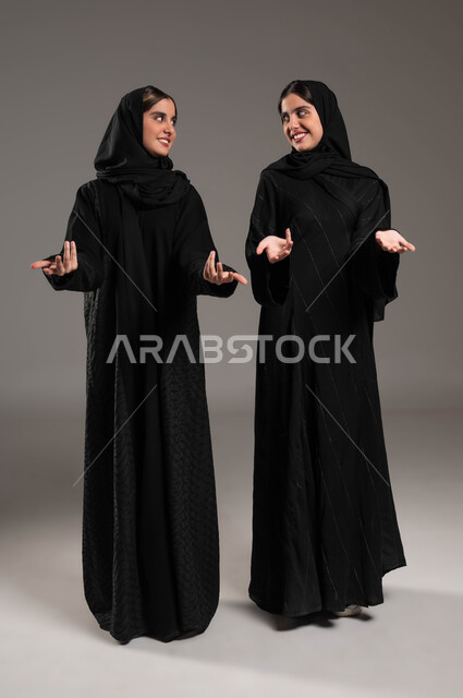 حركات عفوية تدل على امر ما, تعابير الدهشة والتساؤل والحيرة, ايماءات الفرح والسعادة, بورتريه لبنتان توءم عربيتان سعوديتان خليجيتان ترتديان الحجاب والعباءة, النظر الى بعضهم البعض, صورة الجسم بالطول الكامل, خلفية ملونة
