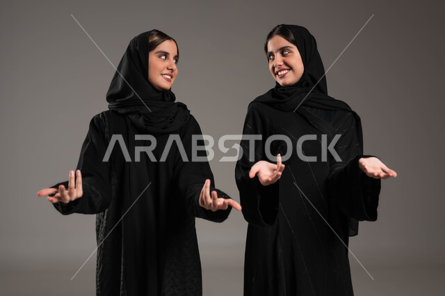 تعابير الدهشة والتساؤل والحيرة, ايماءات الفرح والسعادة, حركات عفوية تدل على امر ما, بورتريه مقرب لبنتان توءم عربيتان سعوديتان خليجيتان ترتديان الحجاب والعباءة, النظر الى بعضهم البعض, خلفية ملونة