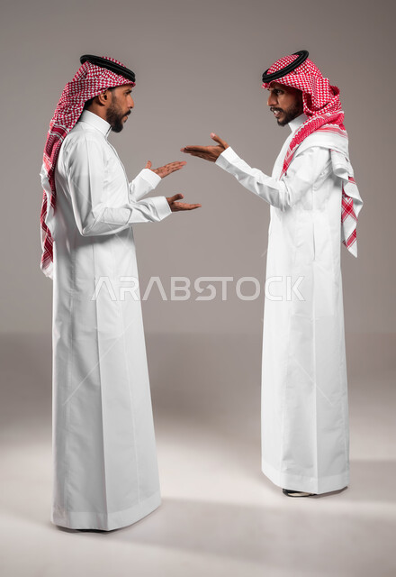 تعابير التعصيب والتوتر الانفعالي، مفهوم النقاش الحاد والمواجهة بين الأخوة، محاولة حل المشاكل العائلية، بورتريه لشابين توءم عربيين خليجيين سعوديين يقفان مقابل بعضهما ويتجادلان بإيماءات الغضب وإلقاء اللوم، صورة الجسم بالكامل، خلفية رمادية