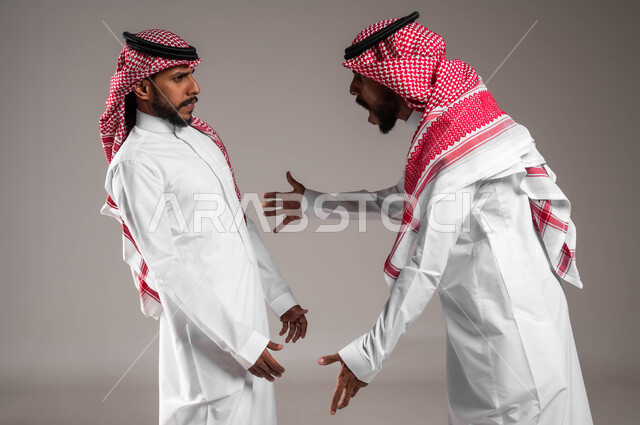 تأثير العواطف السلبية بين الأخوات ،رفع اليدين بإيماءات الصراخ و التوبيخ، بورتريه لرجلان توءم عربيان خليجيان سعوديان يقفان مقابل بعضهما، الغضب والقاء اللوم، النقاش والمواجهة بين الأخوة، الضغط العصبي و التوتر، خلفية بيضاء