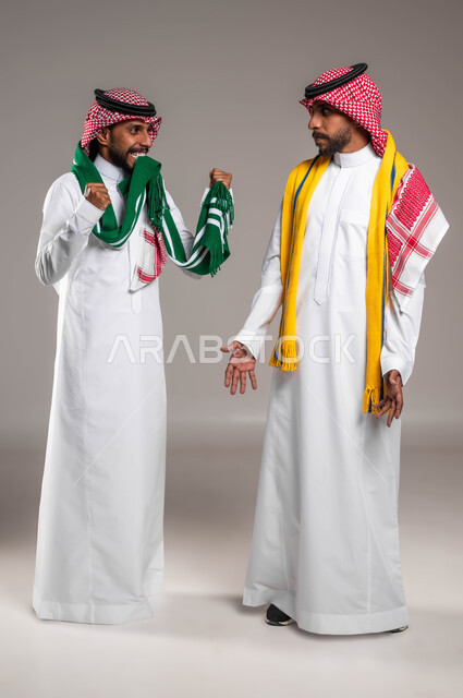تعابير الفرح بالفوز والنصر, المباريات والأنشطة الرياضية, بورتريه لشاب عربي خليجي سعودي يرتدي الثوب التقليدي والشماغ يقوم بإغاظة أخيه التوءم لفوز فريقه المفضل, الوقوف بحزن لخسارة الفريق الرياضي, ارتداء الأوشحة التشجعية, صورة الجسم بالطول الكامل, خلفية رمادية