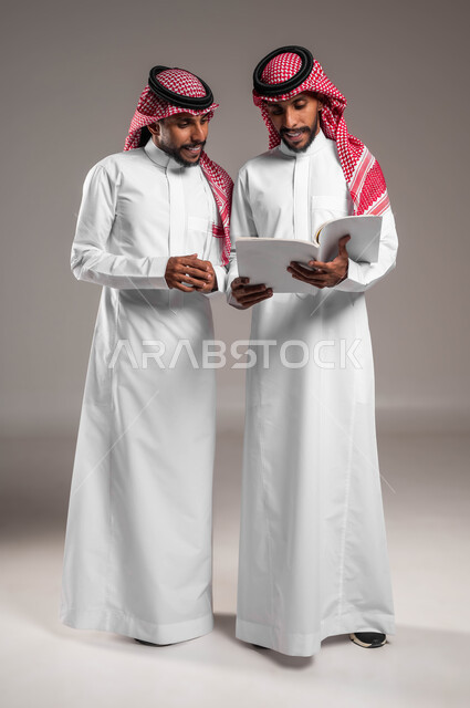 مراجعة الدروس اليومية، ثقافة التعلم الذاتي، الاستمتاع بممارسة هواية المطالعة، بورتريه لشابين توءم عربيين خليجيين سعوديين  مبتسمتين يقضيان وقتهما بالقراءة والتثقف، صورة الجسم بالطول الكامل، خلفية رمادية