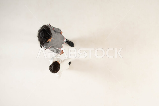 ايماءات السير والذهاب لقضاء أوقات ممتعة مع الأخوات, تعزيز وتقوية العلاقة الإيجابية بين الأخوة, بورتريه علوي عامودي لأخويين عربيين سعوديين خليجيين يمسكان بيد بعضهما, مفهوم الألفة والمحبة والترابط الأخوي, خلفية بيضاء