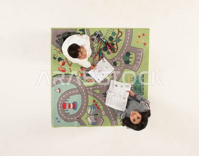 مشاركة النشاطات الترفيهية مع الأخوات, قضاء أوقات الفراغ بممارسة الهوايات الممتعه, بورتريه علوي عامودي لأخوين عربيين خليجيين سعوديين يجلسان على سجادة بتصميم عصري ينظران إلى الكاميرا, تنمية المهارات الحركية والفنية ودعم المواهب, خلفية بيضاء