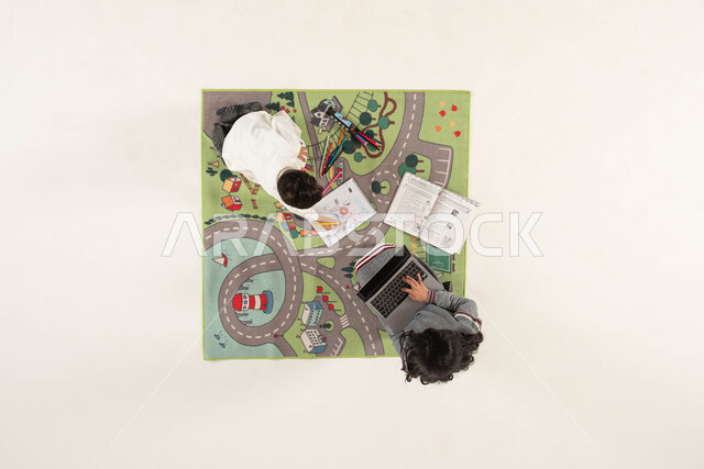 البحث عن معلومة ما عبر الانترنت, الاستمتاع بقضاء وقت ممتع ومفيد مع الأخوة, بورتريه علوي عامودي لولد وبنت عربين خليجين سعوديين إحداهما يقوم بالرسم والتلوين والأخرى تستخدم الحاسب المحمول, تنمية المهارات الفنية لدى الأطفال, خلفية بيضاء