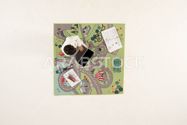 استخدام الأجهزة والتقنيات الحديثة، التعلم وتلقي الدروس عن بعد، بورتريه علوي عامودي لولد عربي خليجي سعودي يرتدي الزي التقليدي يجلس على سجاد بتصميم عصري يستخدم جهاز الحاسوب المحمول، دمج العملية التعليمية مع التقنية و التكنولوجيا, خلفية بيضاء