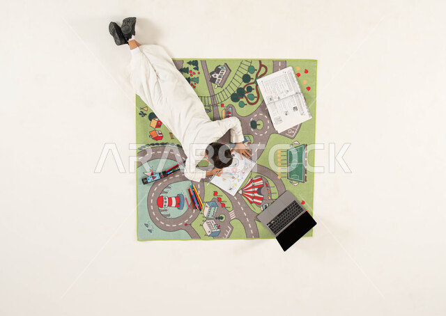 انشطة ترفيهية ممتعة للاطفال، استخدام أدوات الرسم والتلوين وتقوية الإبداع الفني لدى الأبناء، بورتريه علوي عامودي لولد عربي خليجي سعودي يرتدي الزي التقليدي يجلس على سجاد بتصميم عصري يقوم بحل الواجبات، دمج العملية التعليمية مع التقنية والتكنولوجيا, خلفية بيضاء