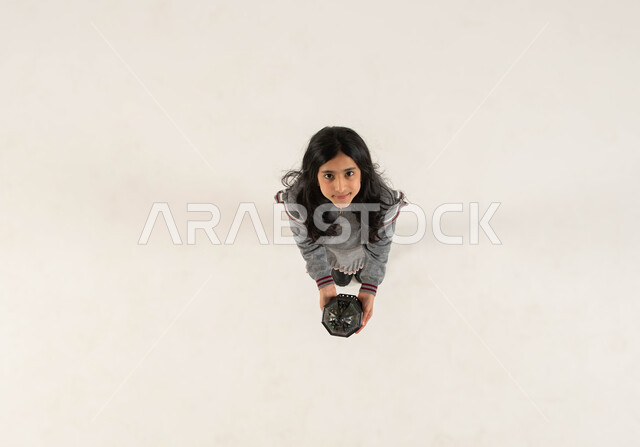 التجهيزات لاستقبال شهر رمضان المبارك، بورتريه علوي عامودي لفتاة عربيه خليجيه سعوديه مبتسمة تحمل بيدها الفانوس المعدني و تنظر الى الكاميرا، المناسبات الدينيه والأعياد الإسلامية، التزيين والتحضير للأجواء الروحانيه الرمضانيه، خلفيه بيضاء.