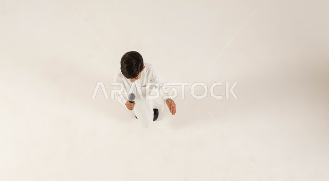 تقديم العروض الفنيه المسرحيه و الغنائيه والفقرات الترفيهية المسليه، بدء التدريب الصوتي، اكتشاف مواهب الغناء عند الاطفال منذ الصغر، بورتريه علوي عامودي لولد عربي خليجي سعودي يمسك بيده المايكروفون، خلفيه بيضاء .