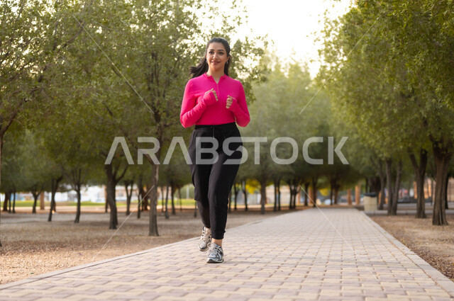 ممارسة هواية الركض و الجري، نشطة ورياضات ترفيهيه شبابيه للمحافظة على الصحه، قضاء وقت العطلة بأمور مفيدة، الاهتمام باللياقة الجسدية و البدنية، امرأة عربية خليجية سعودية ترتدي ملابس رياضية تقضي وقت فراغها في الحديقة، خلفية الطبيعة