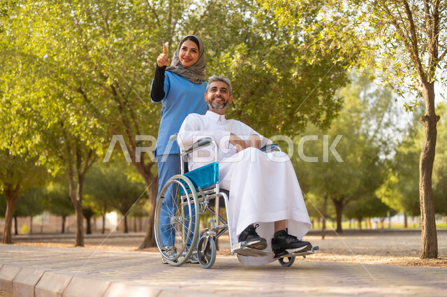 قضاء وقت ممتع بالتجول والتنزه في الحديقة، الاهتمام والرعاية بذوي الاحتياجات الخاصة، تأمين ادوات تساعد أصحاب الهمم على التنقل والحركة، ممرضة عربية خليجية سعودية محجبة تقوم بمساعدة رجل يجلس على الكرسي المتحرك، اسلوب الحياة في السعودية، الاشارة والنظر الى شيء ما