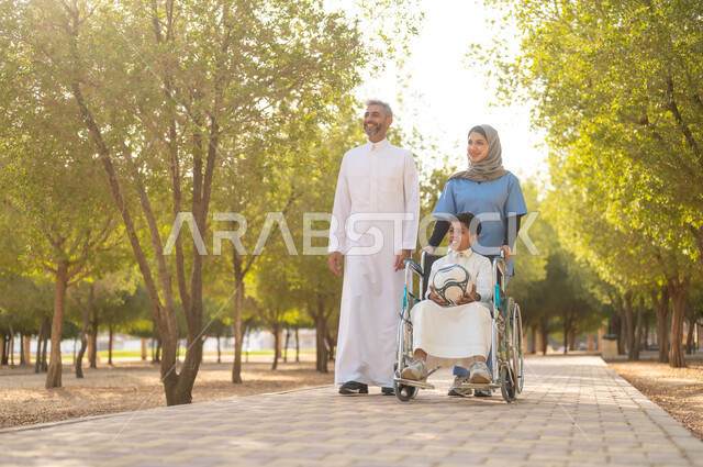 رعاية ذوي الاحتياجات الخاصة، تأمين ادوات تساعد أصحاب الهمم على التنقل، أب يستمتع بالتنزه في إحدى الحدائق في الأجواء الصيفية مع ابنه، الاستعداد للعب بكرة القدم، ممرضة عربية خليجية سعودية محجبة تقوم بمساعدة ولد يجلس على الكرسي المتحرك، نمط الحياة في السعودية