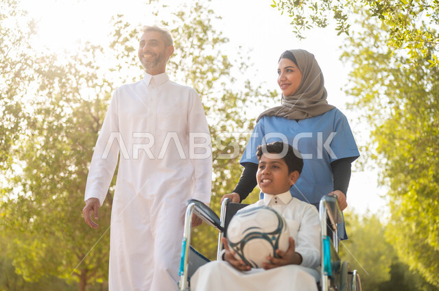 رعاية ذوي الاحتياجات الخاصة، تأمين ادوات تساعد أصحاب الهمم على التنقل، أب يستمتع بالتنزه في إحدى الحدائق في الأجواء الصيفية مع ابنه، الاستعداد للعب بكرة القدم، ممرضة عربية خليجية سعودية محجبة تقوم بمساعدة ولد يجلس على الكرسي المتحرك، نمط الحياة في السعودية