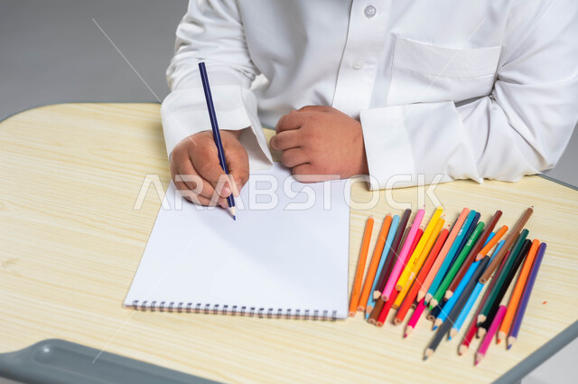 دعم وتنمية المهارة الحركية والفنية للمعاقين, بورتريه ليد شاب عربي خليجي سعودي مصاب بمتلازمة داون يرتدي الثوب التقليدي يمسك أقلام التلوين الخشبية, تمكين ذوي الاحتياجات الخاصة بالمجتمع السعودي, خلفية رمادية