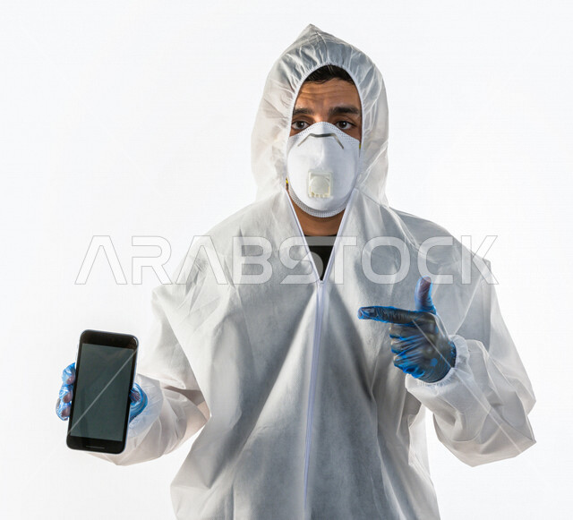 بورتريه لطبيب سعودي يرتدي معدات وقائية لمكافحة فيروس كورونا  ، يرتدي رداء أبيض بلاستيكي قياسي، يرتدي كمامة الوجه  ، تجنب انتشار العدوى ، خلفية بيضاء