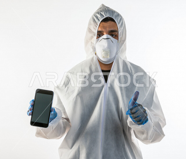 بورتريه لطبيب سعودي يرتدي معدات وقائية لمكافحة فيروس كورونا  ، يرتدي رداء أبيض بلاستيكي قياسي، يرتدي كمامة الوجه  ، تجنب انتشار العدوى ، خلفية بيضاء