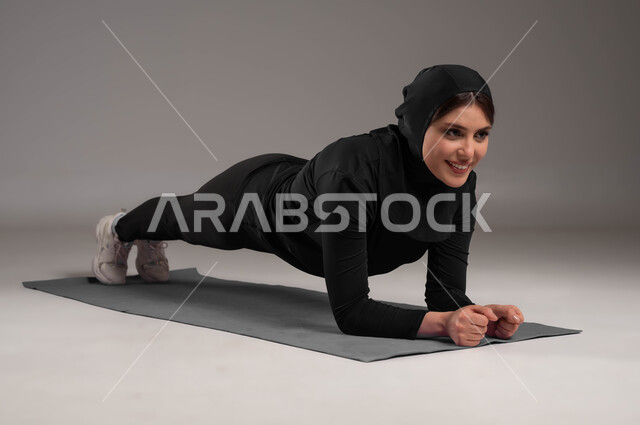 Maintaining physical balance, exercising, a healthy lifestyle, activities and sports to strengthen the muscles and sculpt the body, a portrait of a veiled Saudi Arabian Gulf woman wearing a sports uniform, physical activity to maintain health and body, the concept of agility and fitness, a full-body portrait, gray background