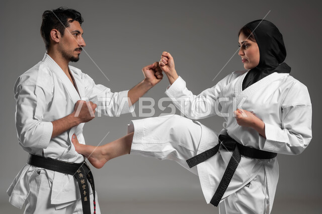 The concept of combat sports, gestures of strength and challenge, martial arts, a close-up portrait of a girl and a young man, two Saudi Gulf Arabs wearing a white karate uniform and a black belt and the young woman wearing a black hijab, education and skills development, gray background